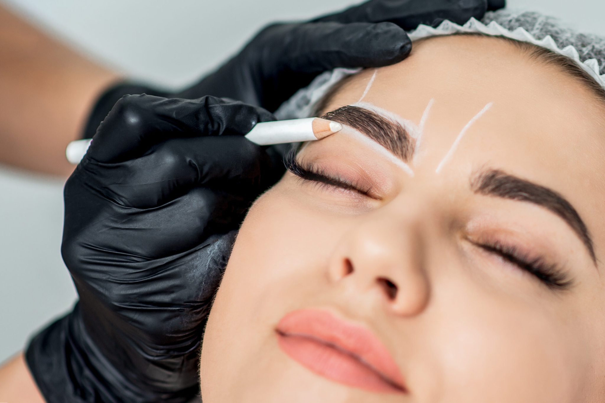 Markup with pencil on eyebrows of young woman while permanent make up.